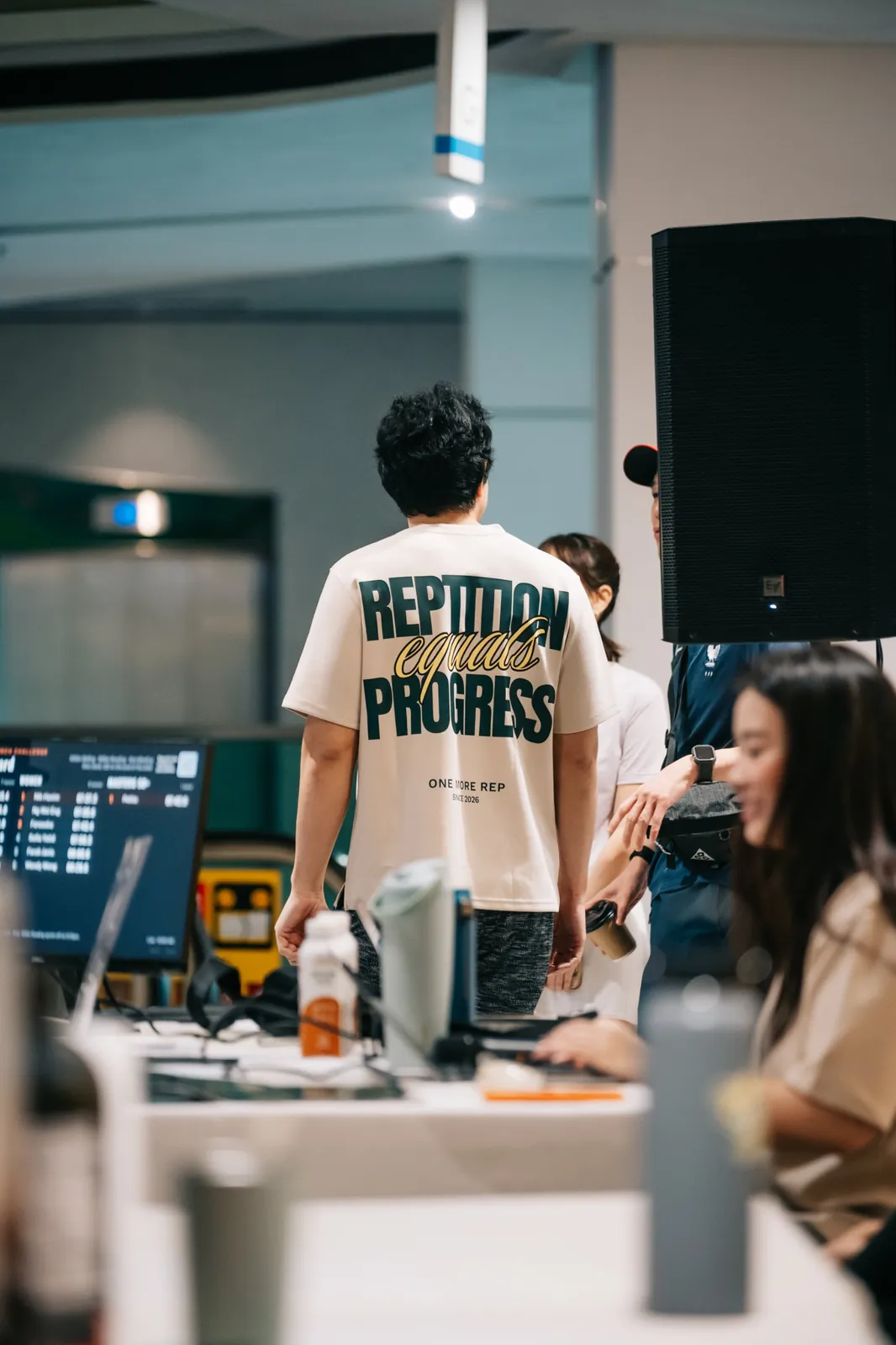 The back of a Repetition Equals Progress tee by the scoreboard