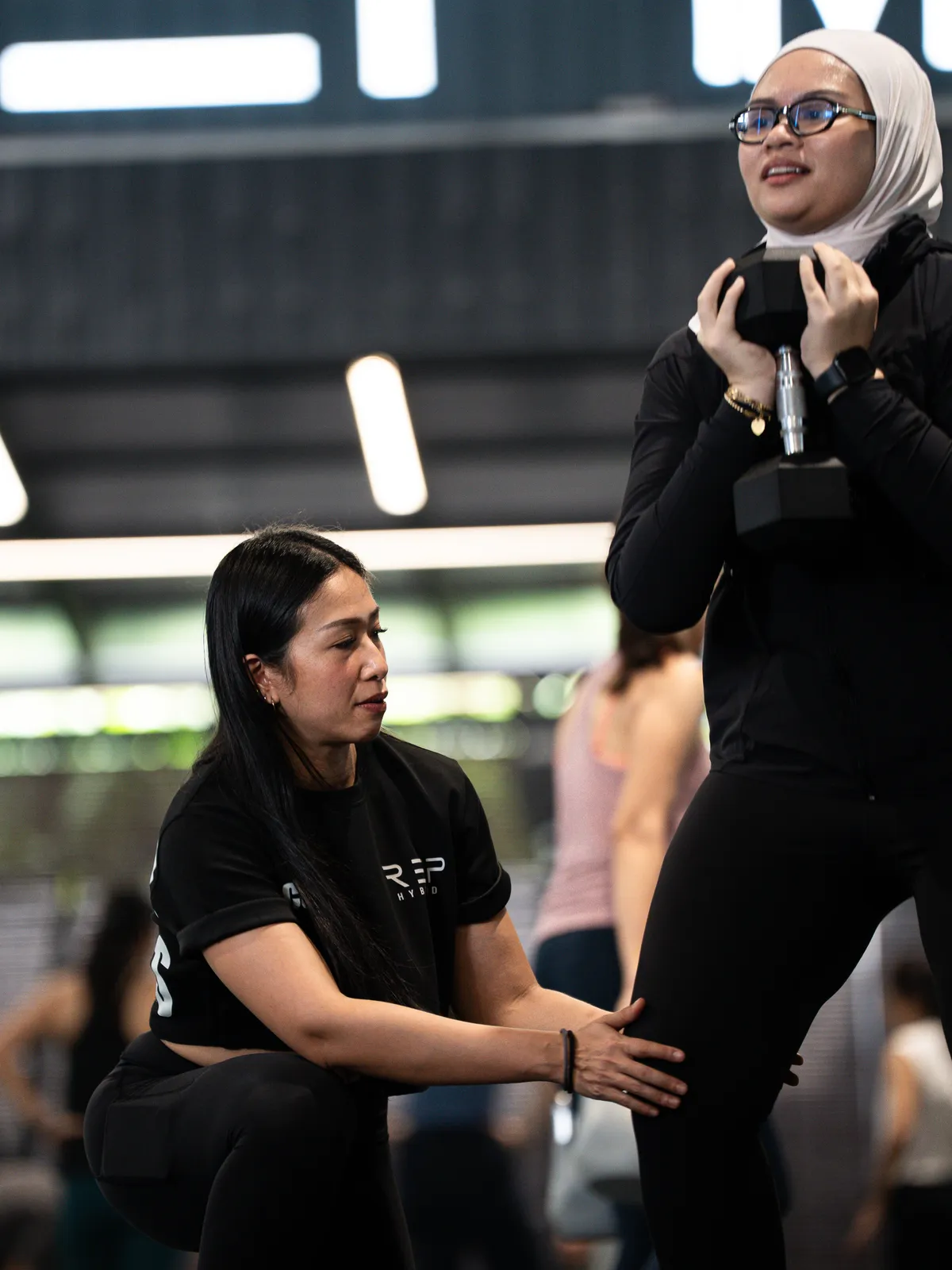 A coach checking a member's knee position in a goblet squat