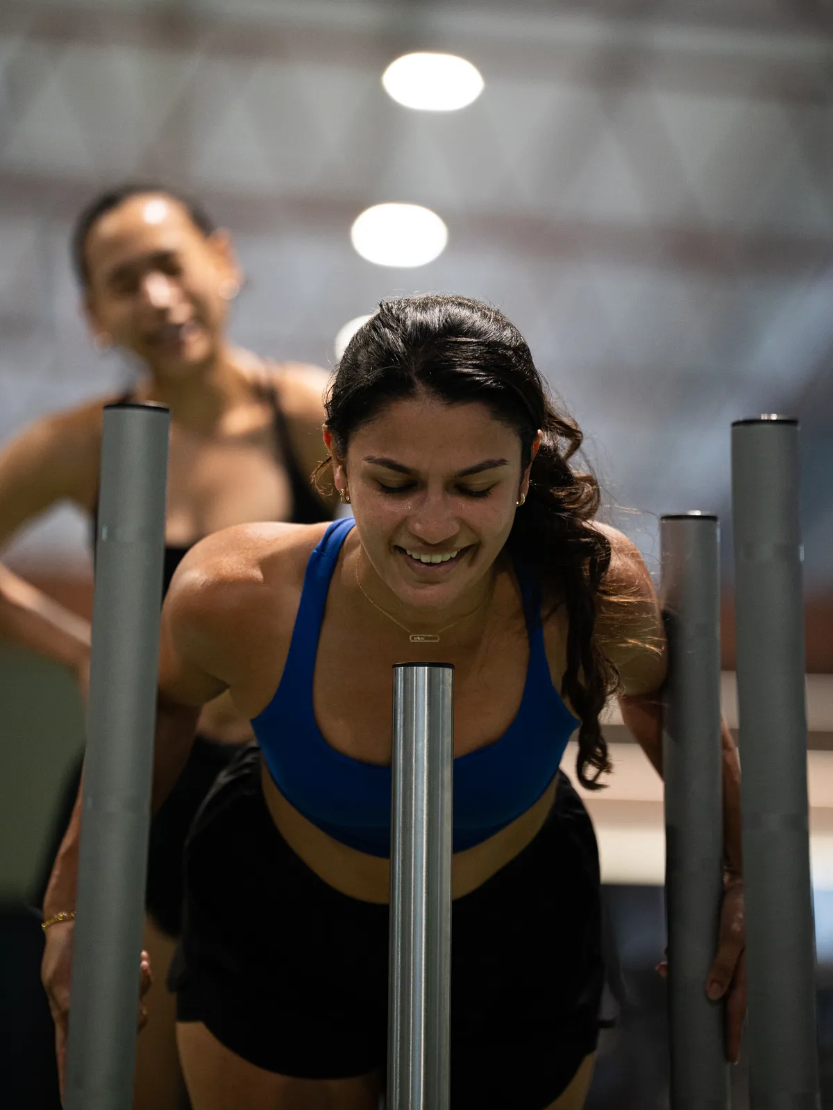 An athlete smiling into a sled push, a friend cheering behind